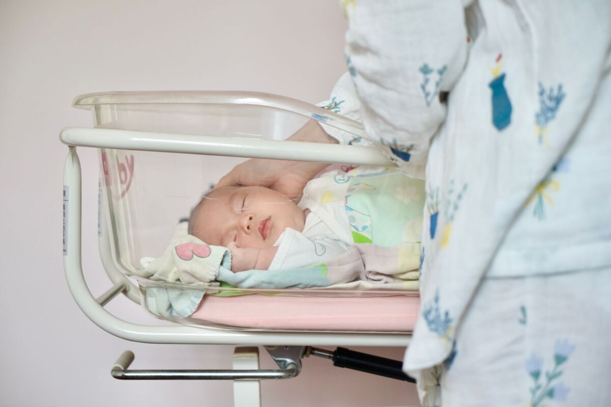 A tender moment of a newborn baby sleeping peacefully in a hospital bassinet being gently touched by a parent.