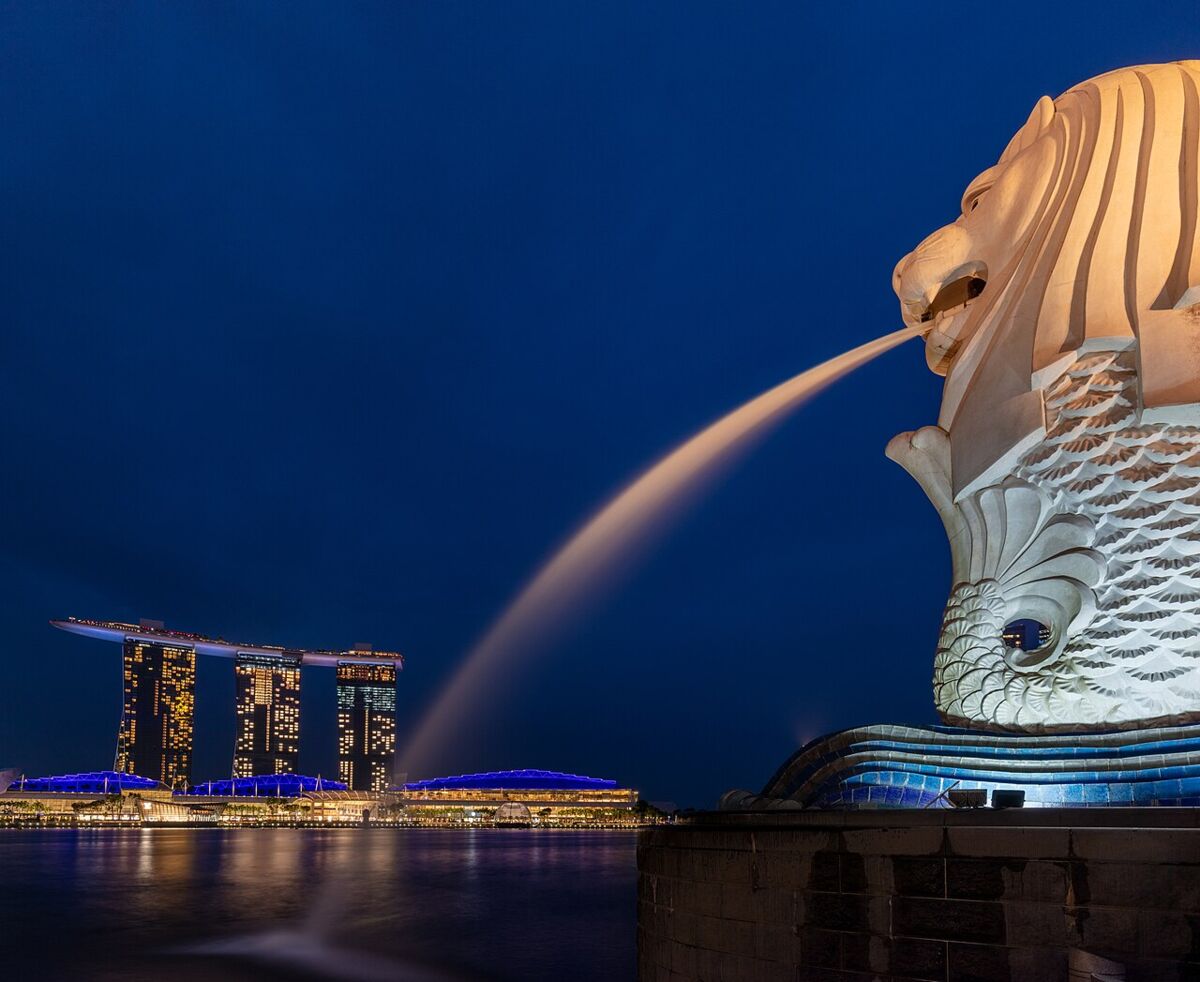 The illuminated Merlion spouting water at blue hour with Marina Bay Sands lit up across the bay