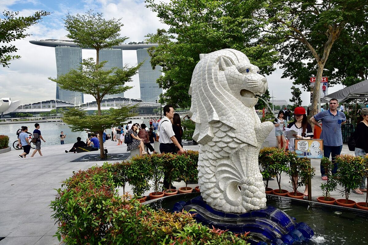 The smaller Merlion cub statue in the landscaped garden at Merlion Park with visitors and Marina Bay Sands behind