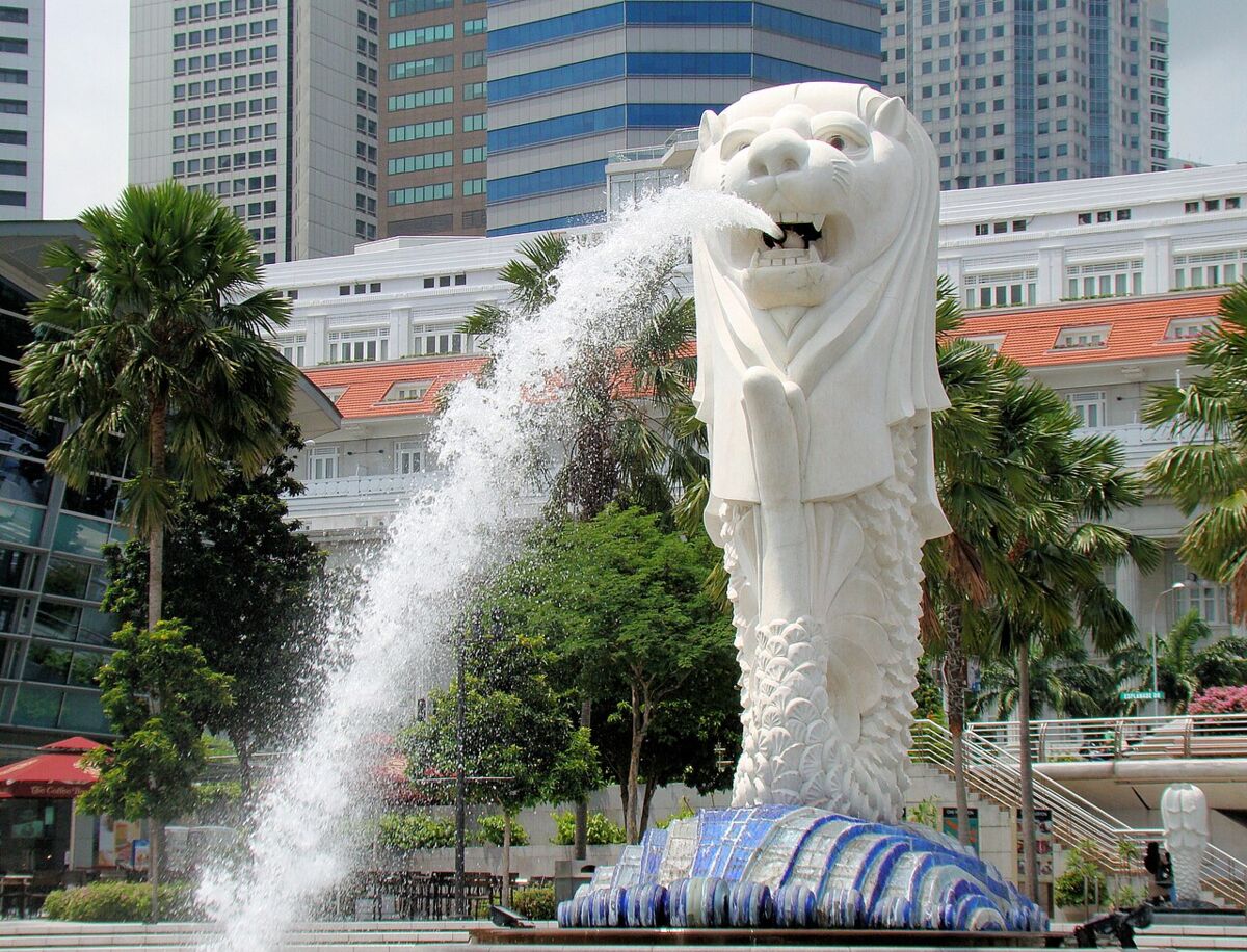 The Merlion statue spouting water framed by palm trees with the colonial Fullerton Hotel in the background
