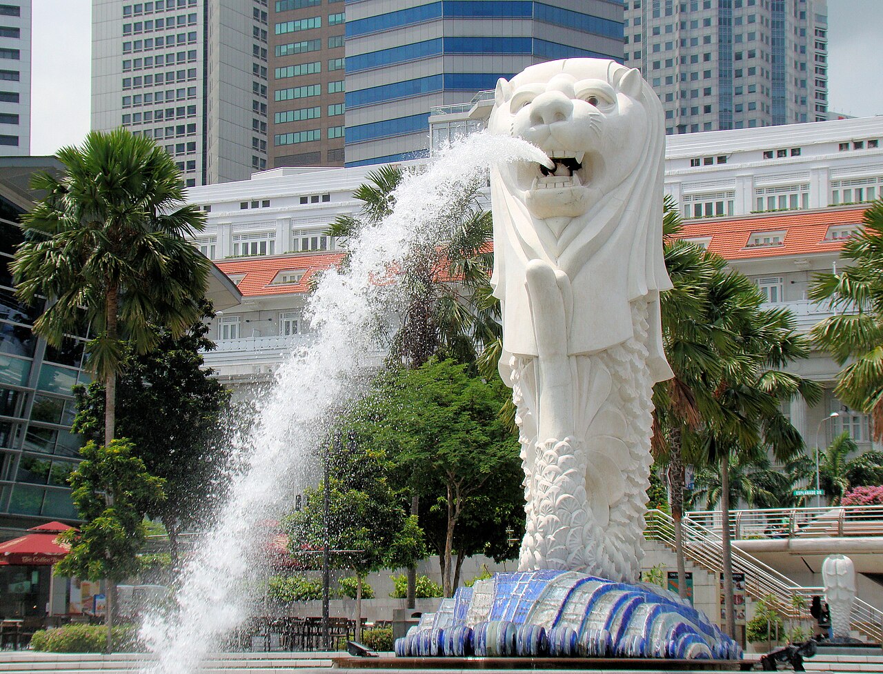 The Merlion statue spouting water framed by palm trees with the colonial Fullerton Hotel in the background