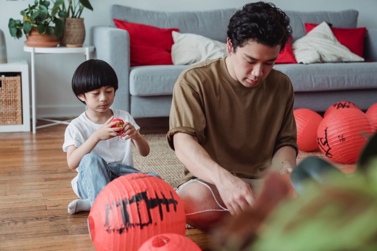 A father and son prepare red paper lanterns in a cozy living room, capturing a moment of cultural bonding.