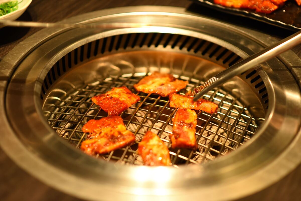 Close-up of sizzling meat pieces on a Korean BBQ grill, captured indoors.