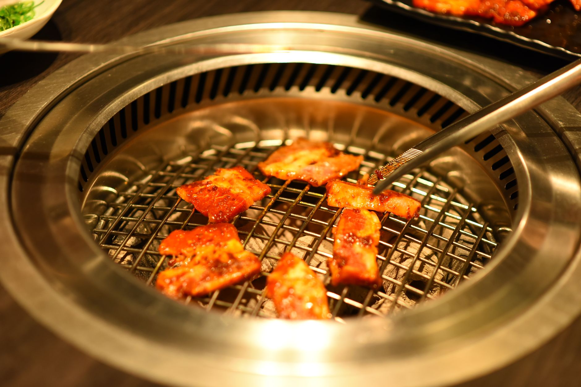 Close-up of sizzling meat pieces on a Korean BBQ grill, captured indoors.