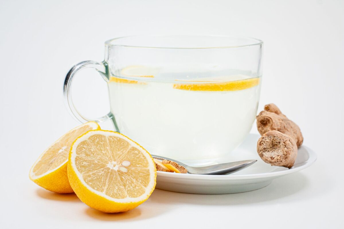 A soothing cup of lemon ginger tea with fresh lemon slices and ginger root on a white background.