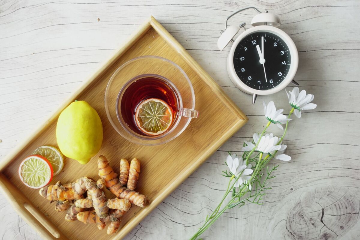 Overhead view of herbal tea with lemon, turmeric, and flowers on wooden tray. Healthy lifestyle concept.
