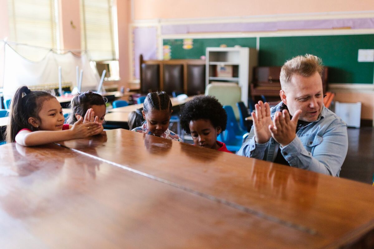 Children clap along with their teacher during an interactive music lesson in a classroom.