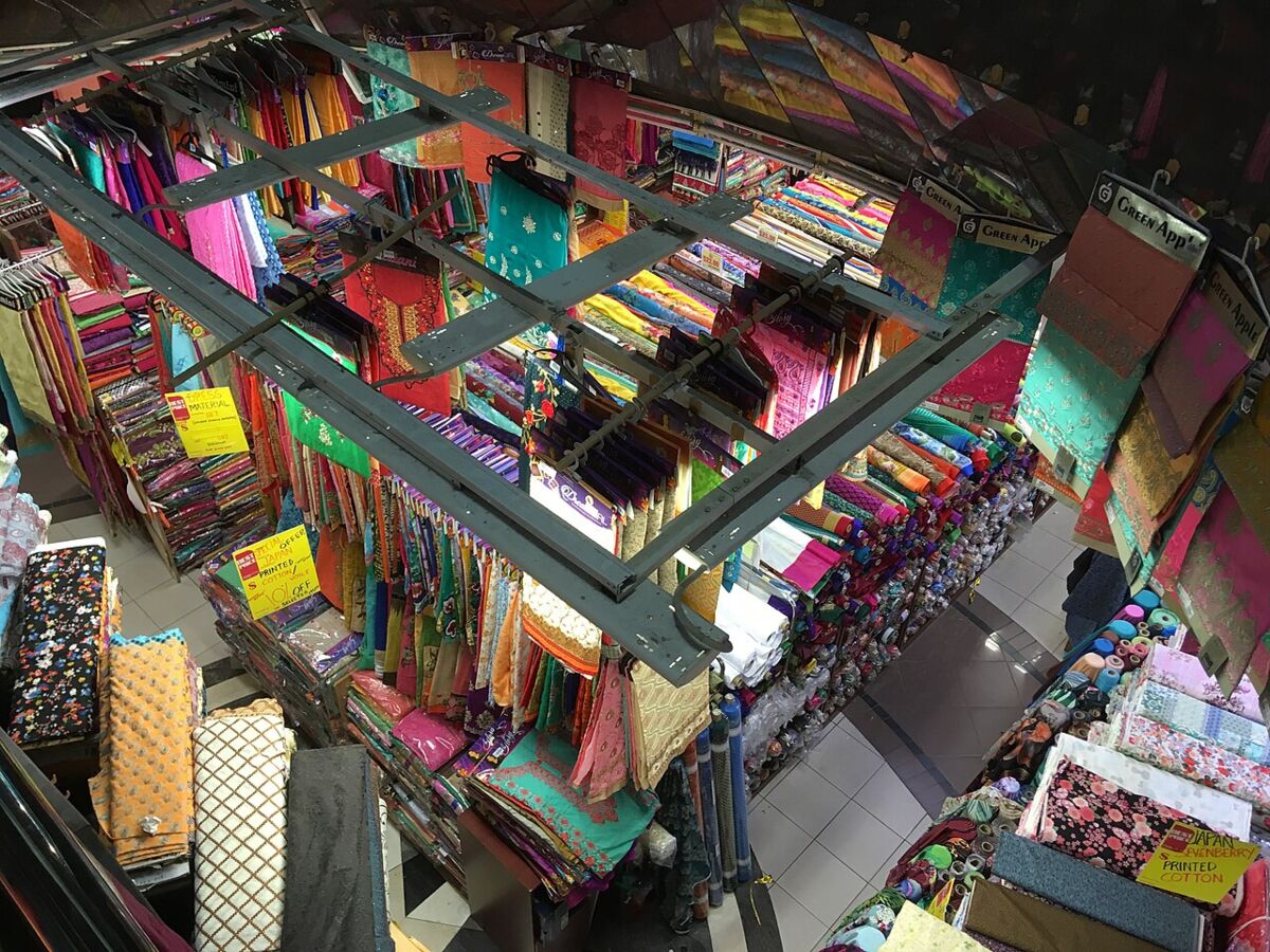 Colourful rolls of fabric and textiles stacked on shelves inside Mustafa Centre, viewed from above