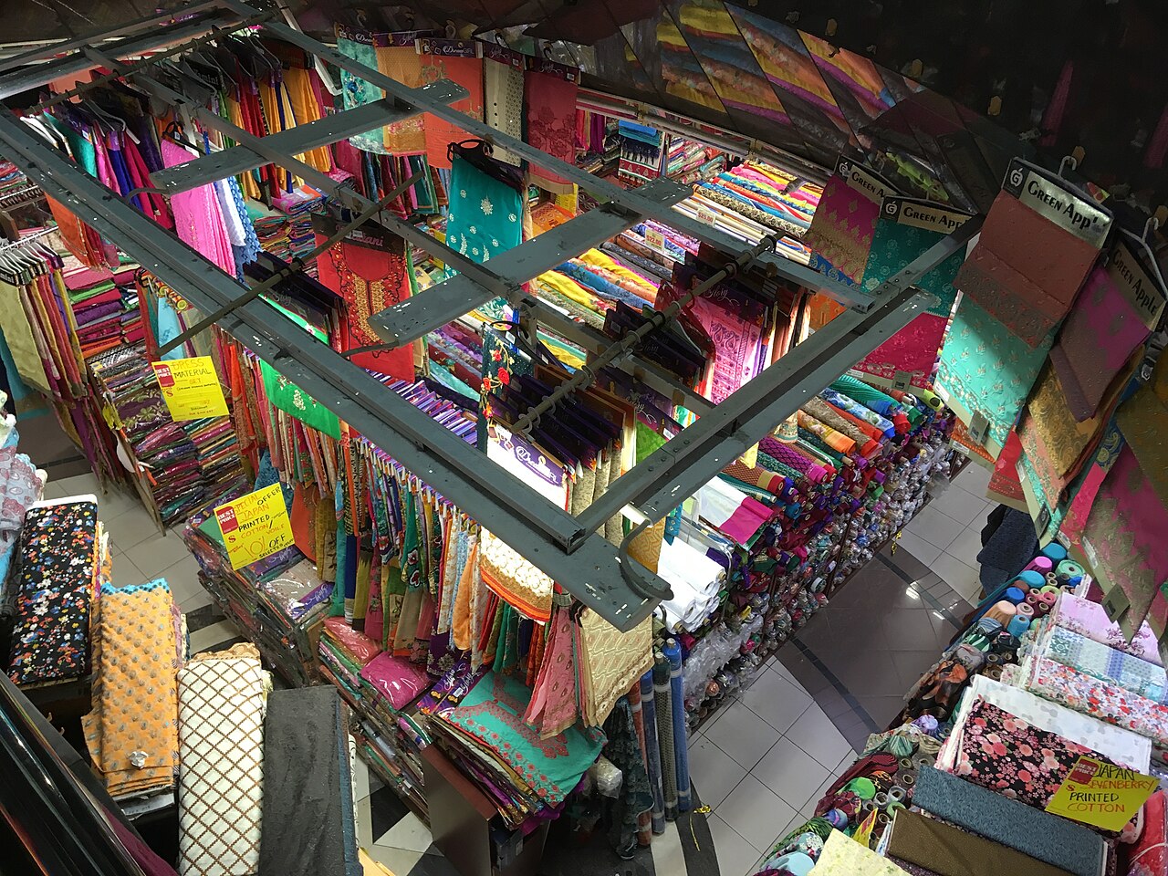 Colourful rolls of fabric and textiles stacked on shelves inside Mustafa Centre, viewed from above