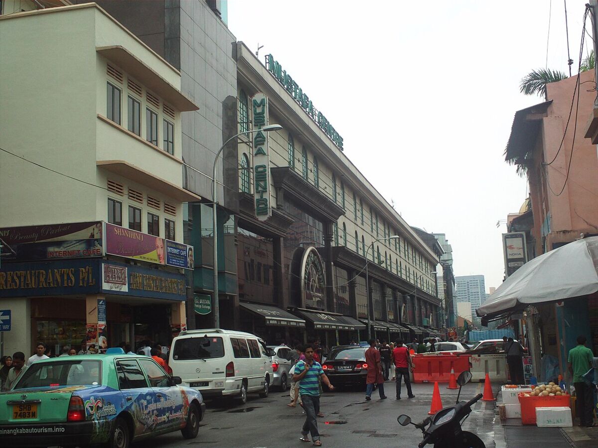 Street-level exterior view of the Mustafa Centre building facade with traffic and shops along the road in Little India