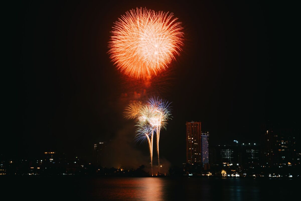 Vibrant fireworks illuminate a city skyline at night, reflecting on the water.