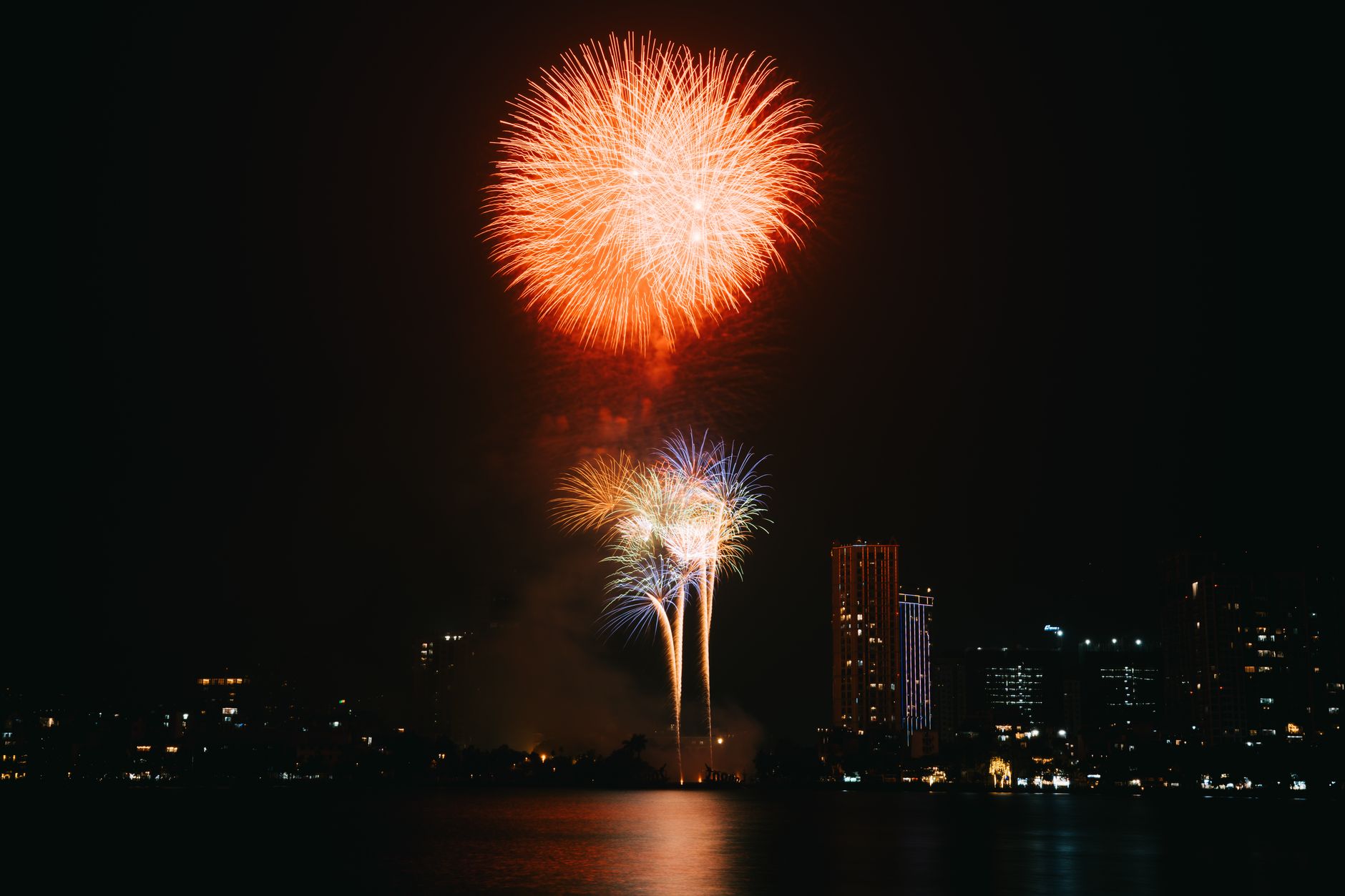Vibrant fireworks illuminate a city skyline at night, reflecting on the water.