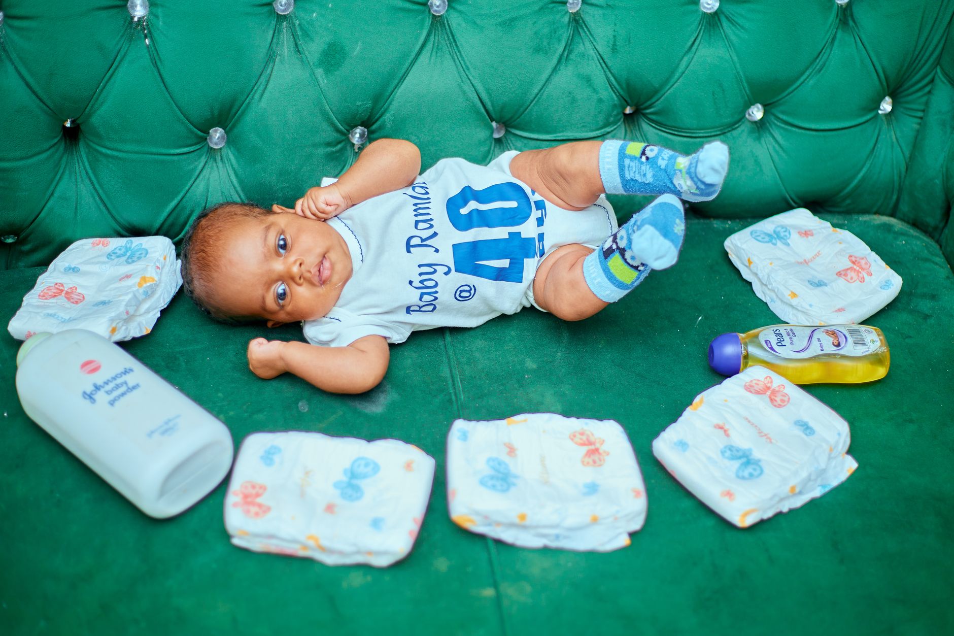 Cute baby lying on a green couch surrounded by diapers and baby care items