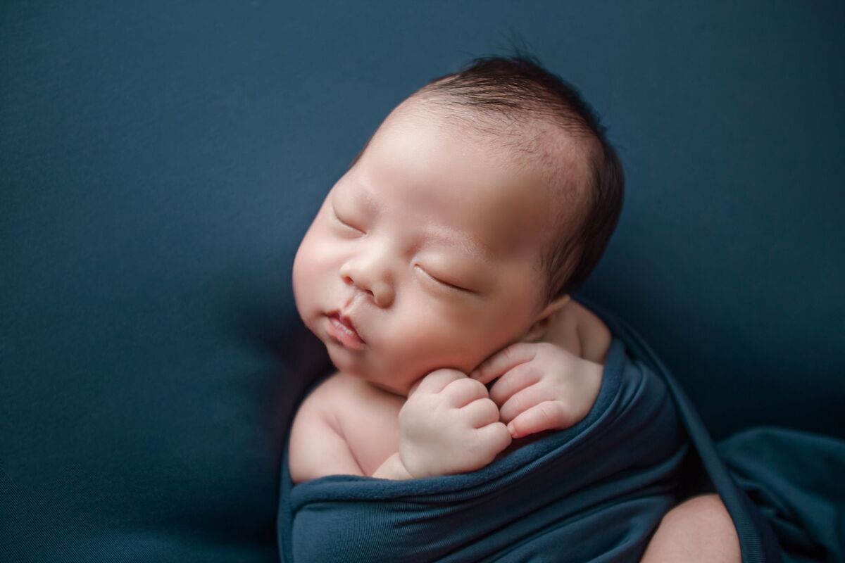 Adorable newborn baby peacefully sleeping, wrapped in a blue blanket, captured in high-quality portrait.