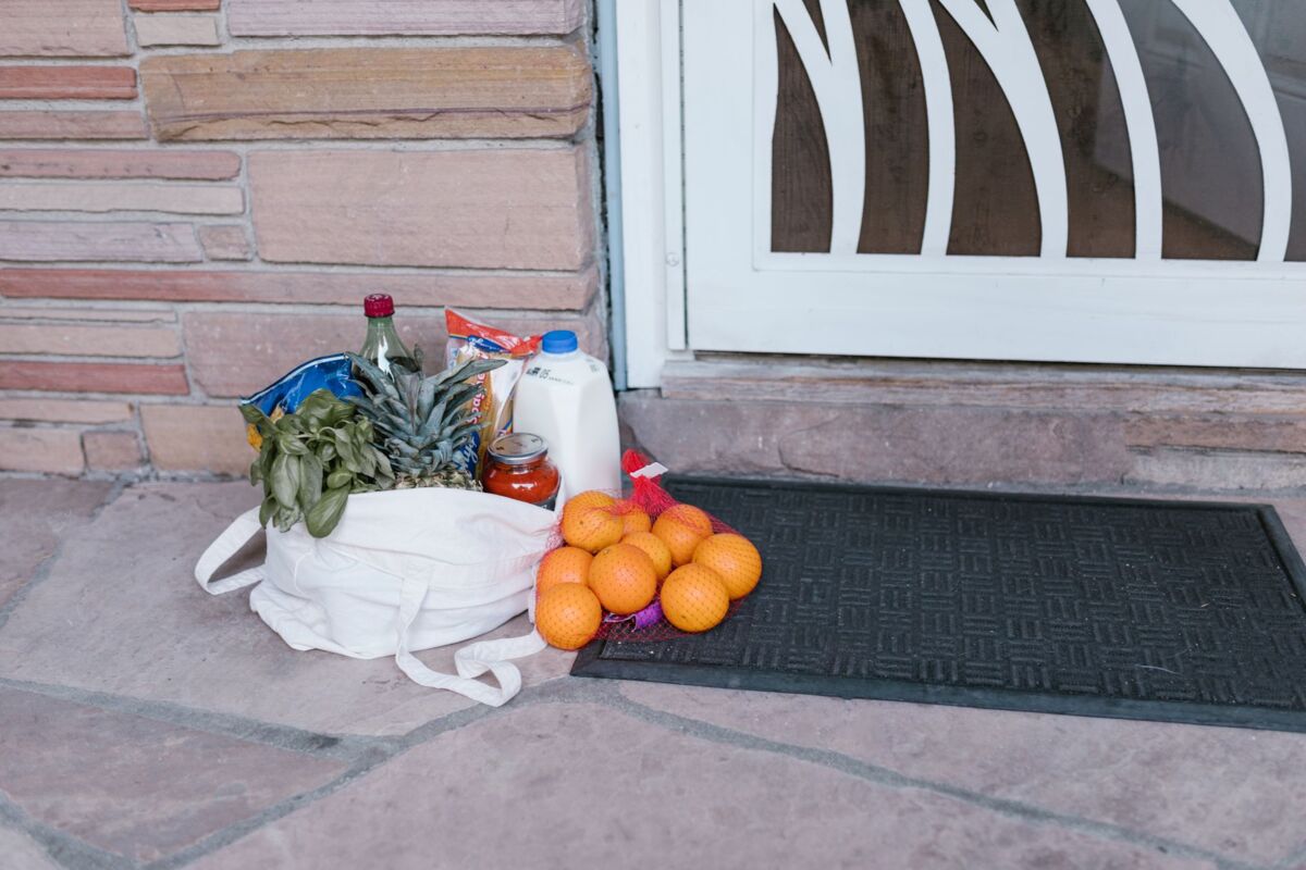 Reusable bag with groceries and fruits left at doorstep, highlighting delivery service.