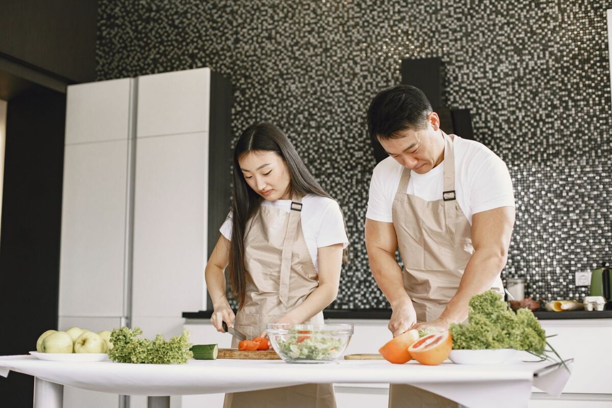 Asian couple preparing healthy meal together in a modern kitchen, slicing fresh vegetables.