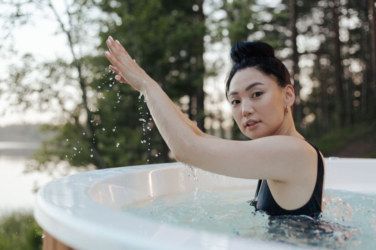 An Asian woman enjoys relaxation in an outdoor hot tub surrounded by nature.