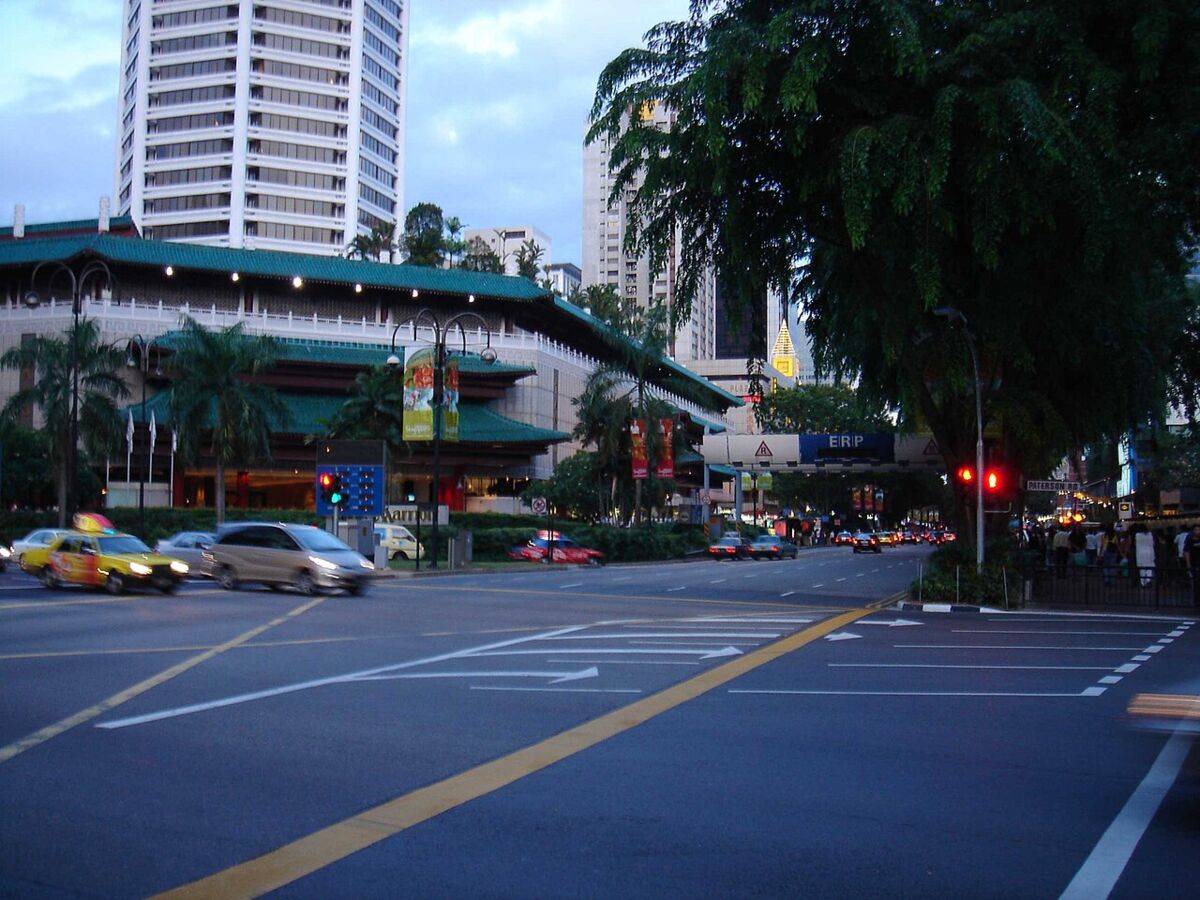 Street view along Orchard Road at dusk with taxis and cars passing a leafy shopping precinct in Singapore