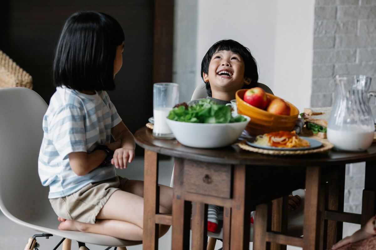 Happy Asian boy and girl sitting at table with bowl of food and milk in kitchen while having breakfast in morning.