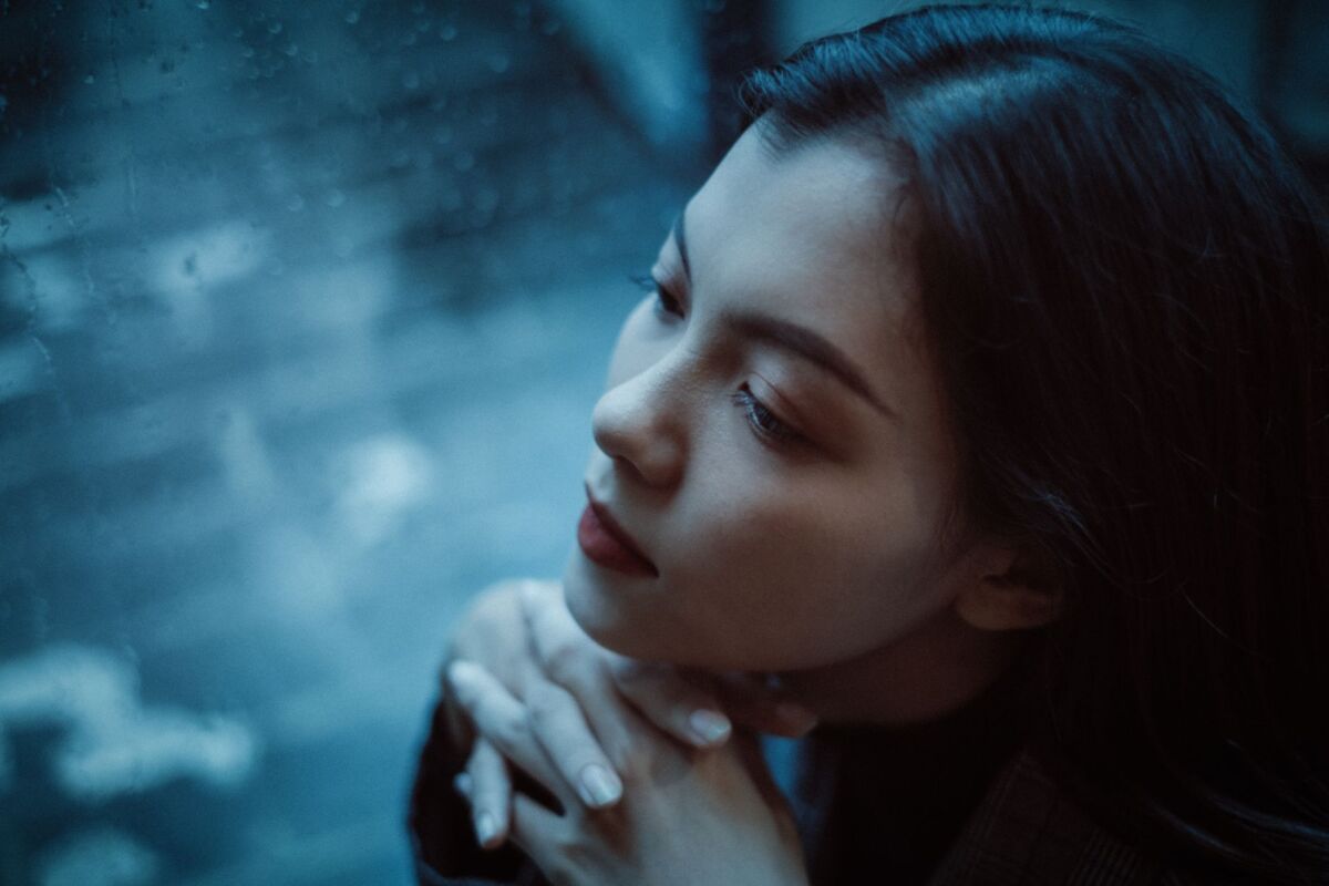 A thoughtful woman looks out a rainy window, deep in contemplation.