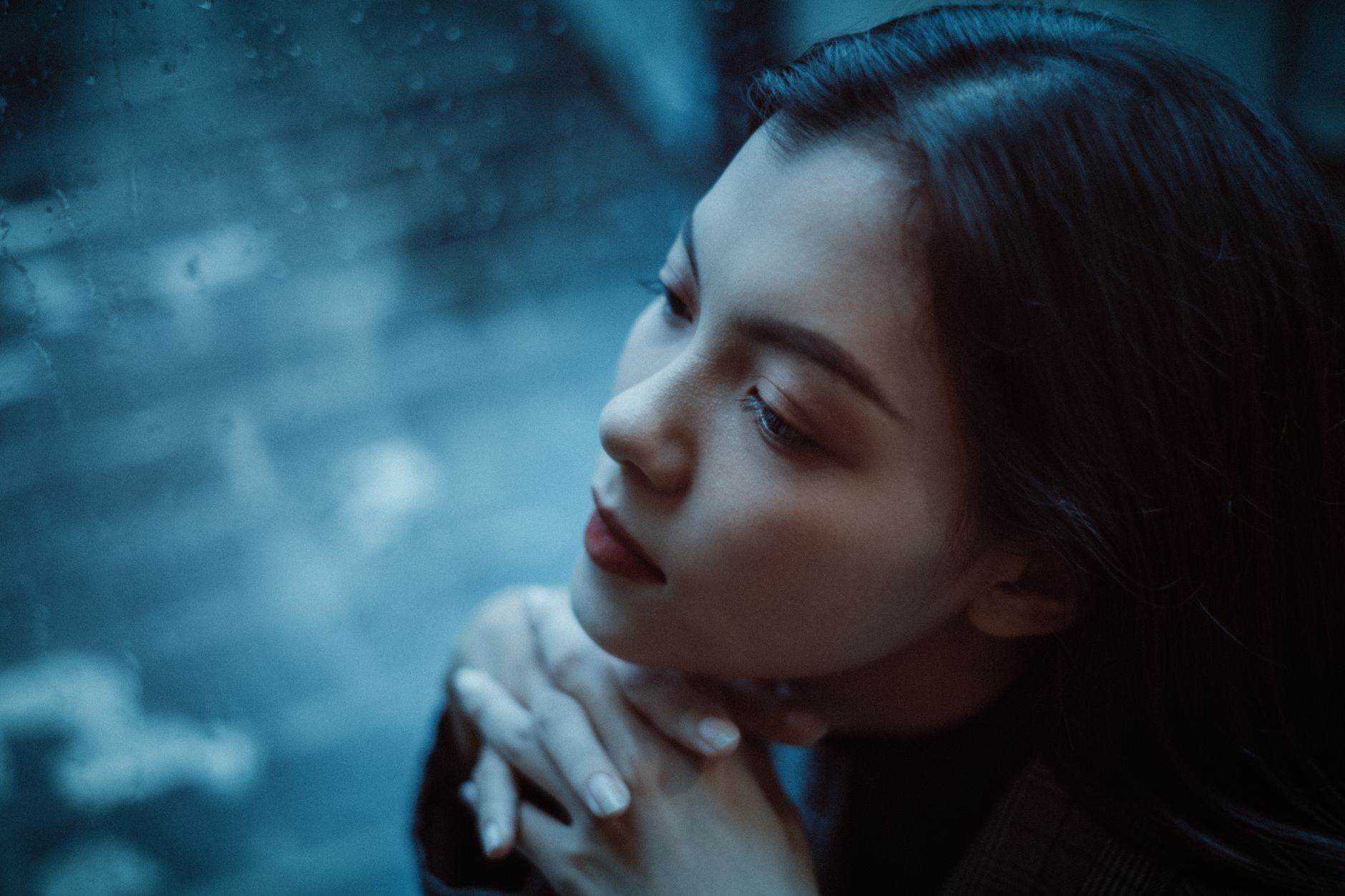 A thoughtful woman looks out a rainy window, deep in contemplation.
