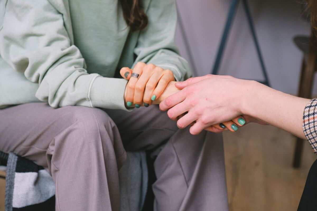 Crop unrecognizable counselor holding hand of woman while speaking during psychotherapy session and sitting in light workspace