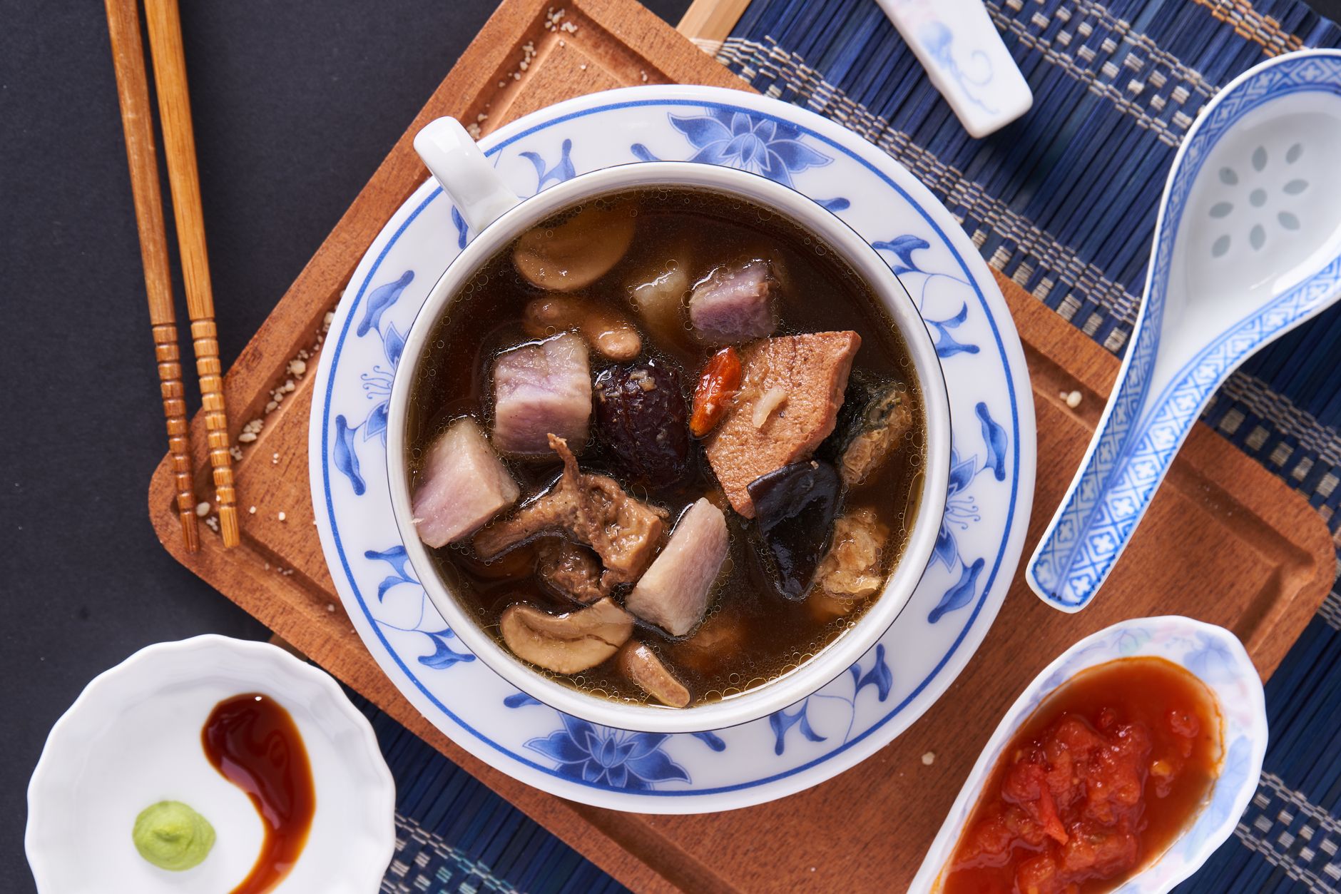 Appetizing Chinese soup with mushrooms, tofu, and soy sauce on a wooden tray.