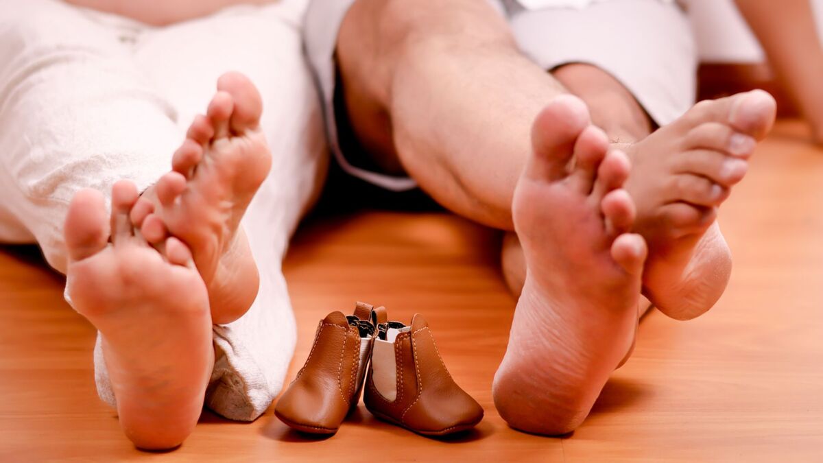 A family's anticipation captured with bare feet and tiny baby shoes on a wooden floor.