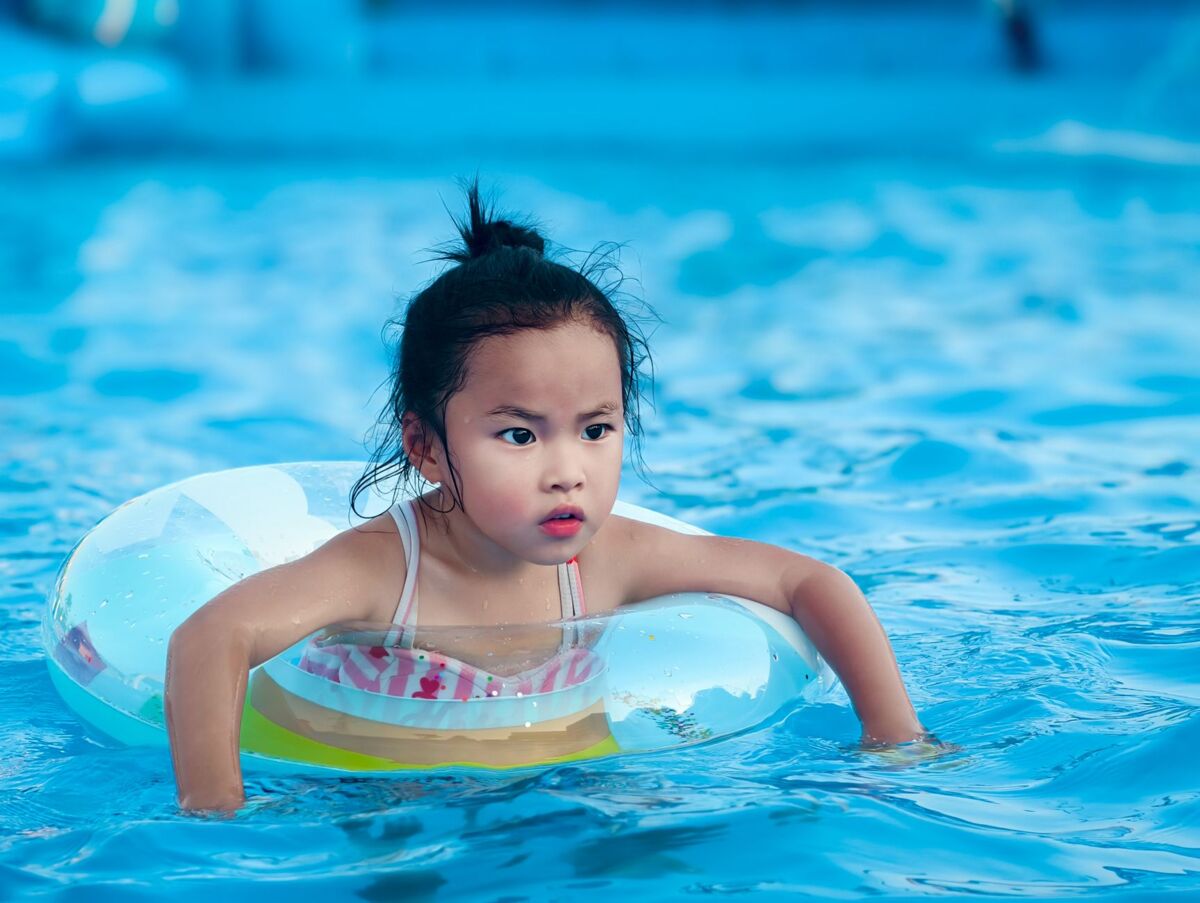 A young child having fun in a pool with an inflatable swim ring on a sunny day.