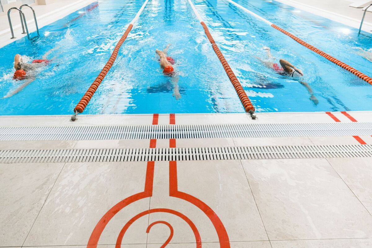 Three athletes swimming freestyle in a bright indoor pool.