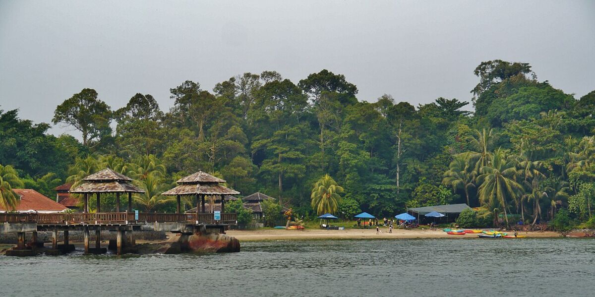Wooden jetty shelters and a beach lined with colourful kayaks at Pulau Ubin, backed by dense jungle