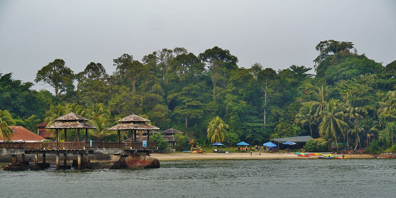 Wooden jetty shelters and a beach lined with colourful kayaks at Pulau Ubin, backed by dense jungle