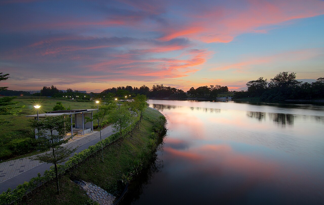 Pink and orange sunset reflected in the calm Punggol Waterway beside a lit riverside path