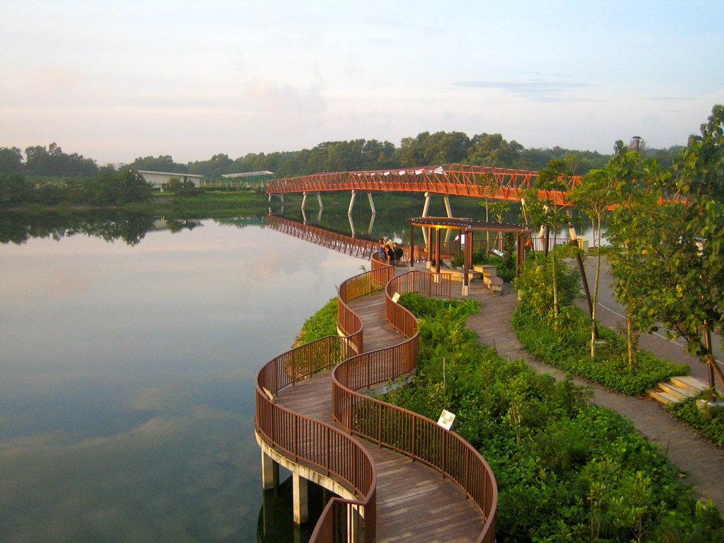 Curving wooden boardwalk and red Jewel Bridge over the calm water at Punggol Waterway Park