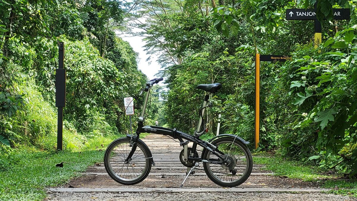 Bicycle on a shaded forested stretch of the Rail Corridor trail beside a directional signpost