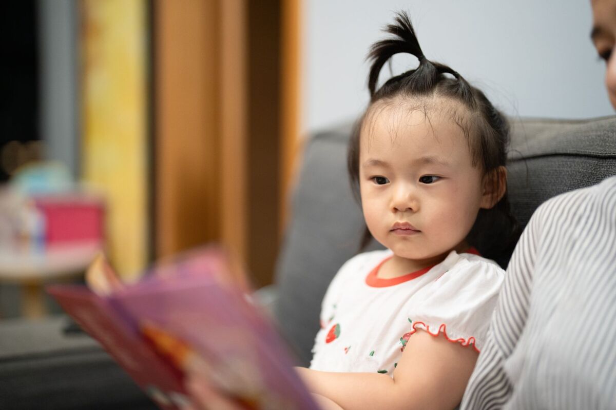 A young child on a sofa attentively listening during a reading session indoors.