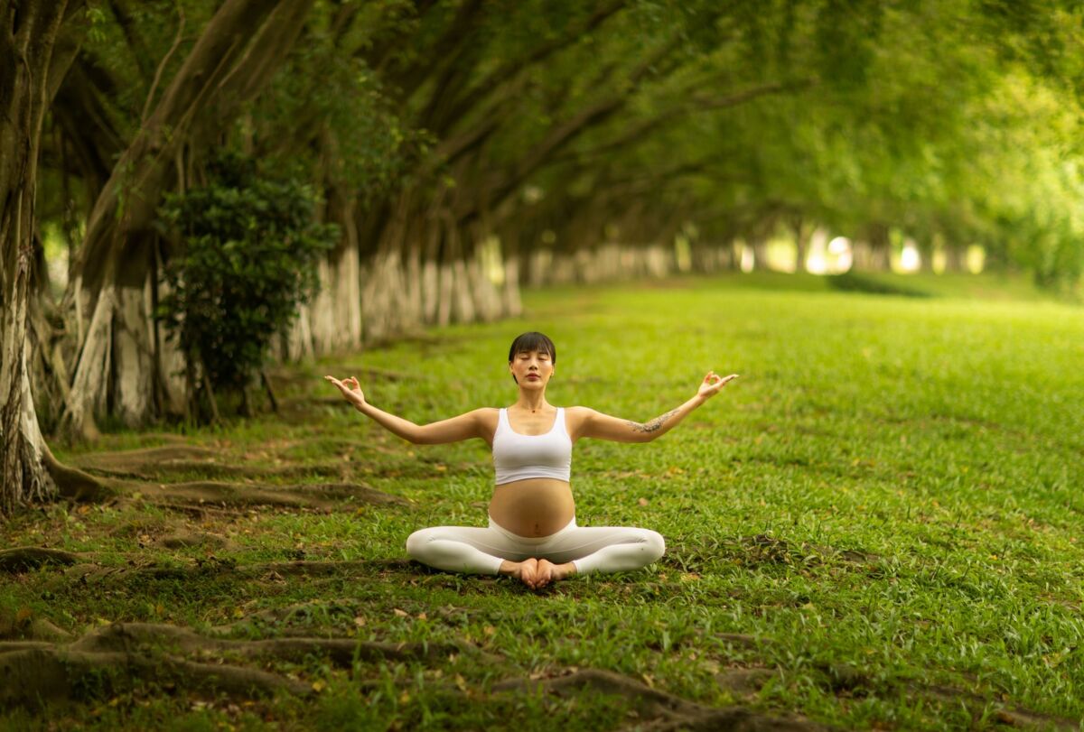 Pregnant woman meditating on the grass, embracing wellness and tranquility outdoors.