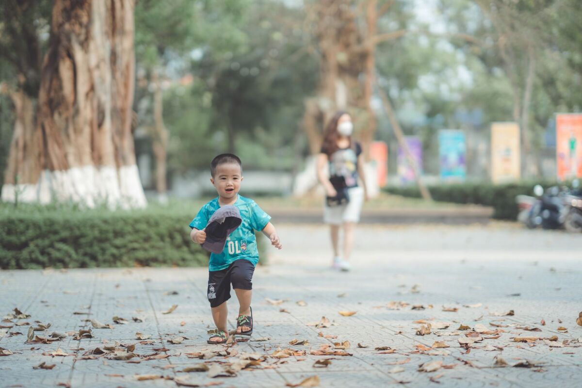 Asian boy in a blue shirt joyfully running in a sunlit park during daytime.