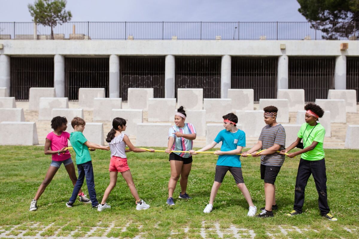 Group of kids playing tug of war outdoors at summer camp, enjoying a fun team building activity.