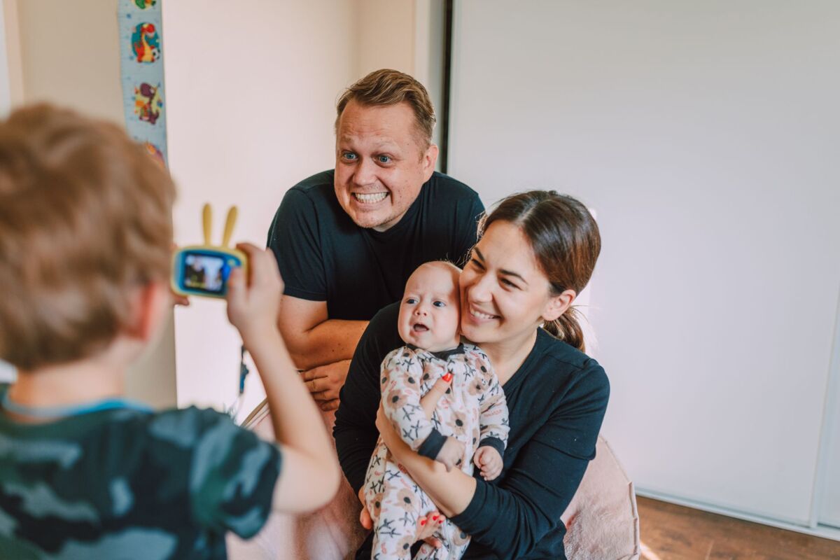 A joyful family with a child capturing a moment using a toy camera indoors.