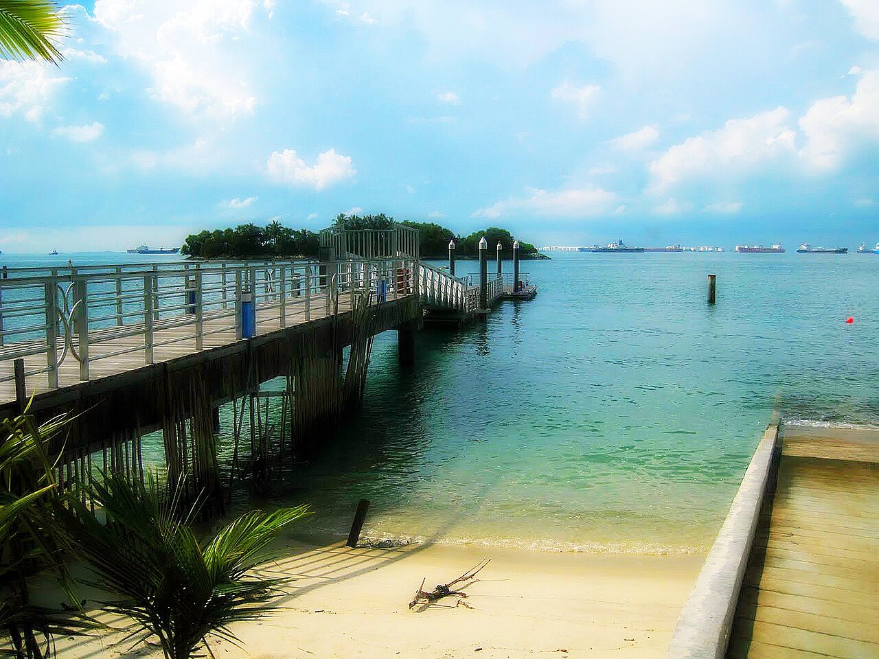 Wooden boardwalk jetty over clear shallow water leading to a small islet at Sentosa beach