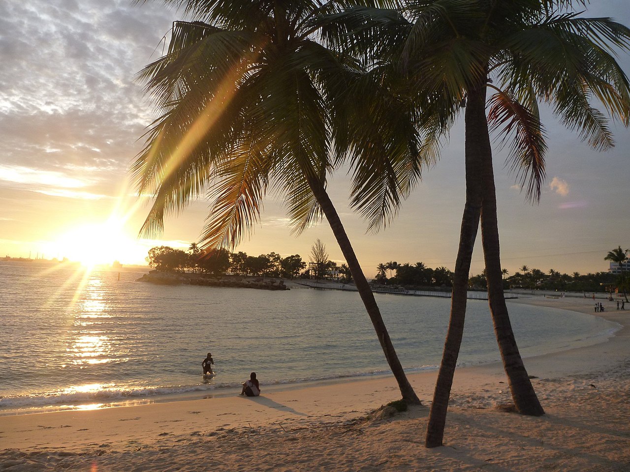 Sunset over a Sentosa beach with palm trees and people on the sand