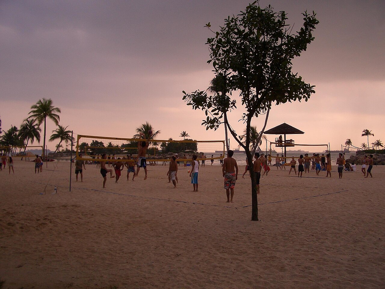 People playing beach volleyball on the sand at Sentosa at dusk