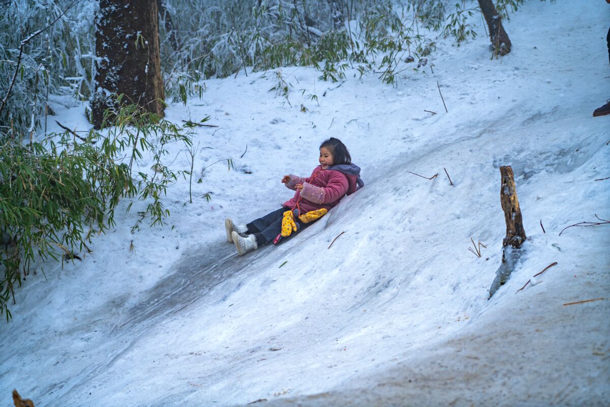 A child in a red jacket enjoys sliding down a snowy hill in Leshan, China.