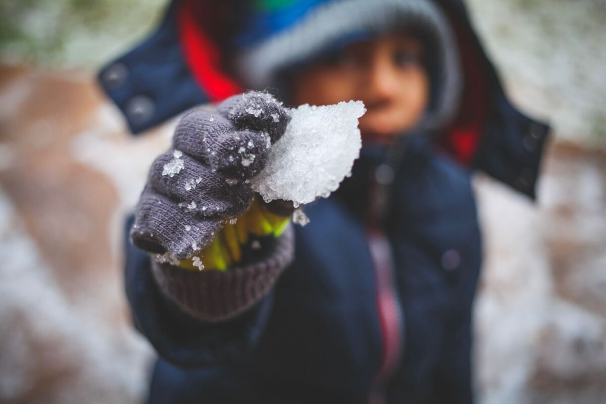 A child in winter attire holds a piece of snow in a mittened hand, highlighting winter fun.