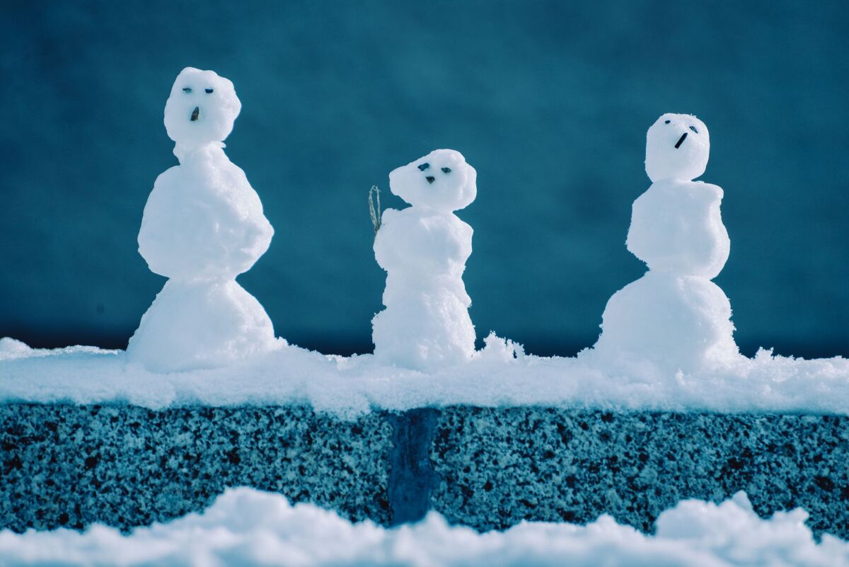 Charming trio of small snowmen on a snowy wall, symbolizing winter joy and creativity.