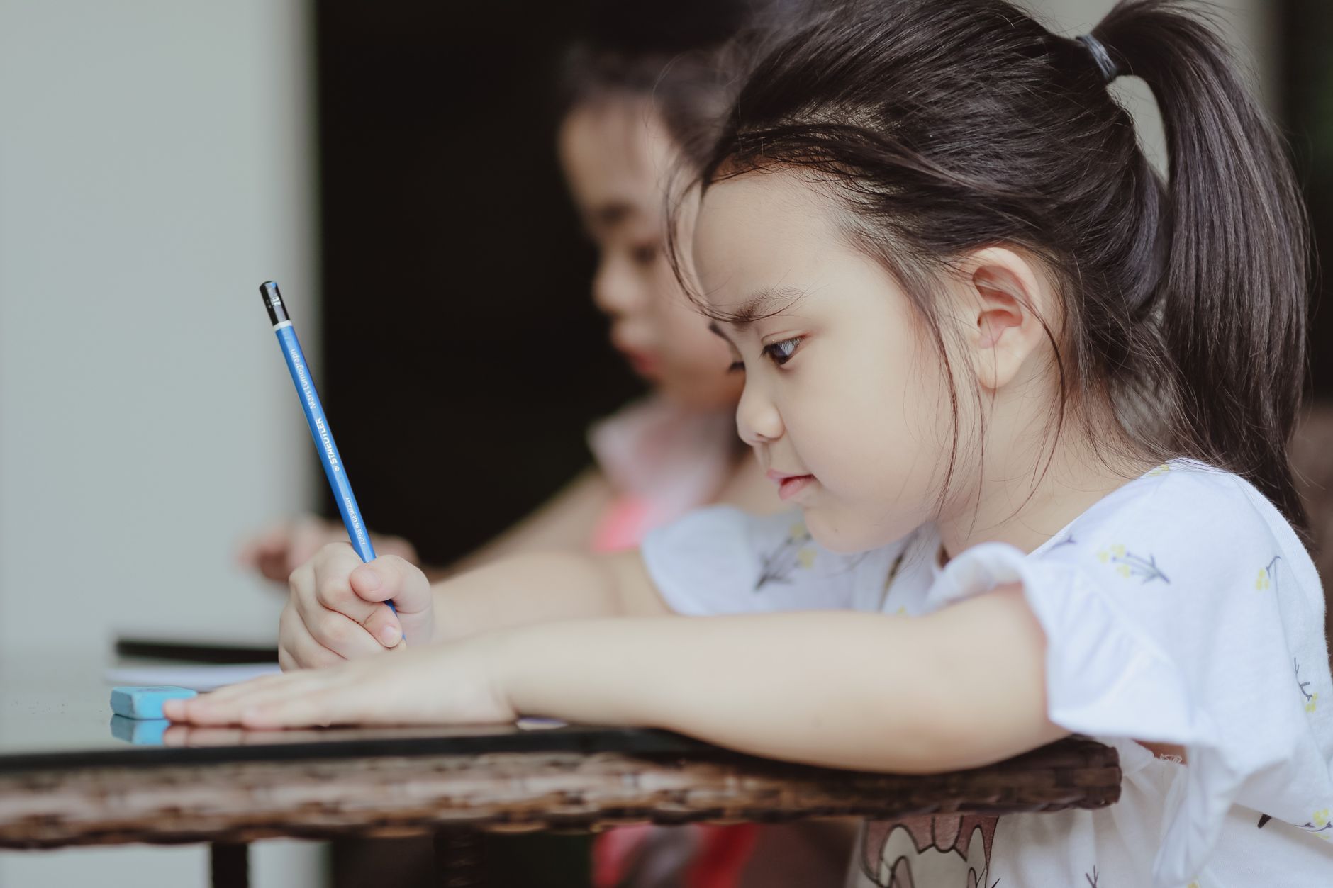 Adorable little Asian child girl drawing with pencil sitting at table in kindergarten