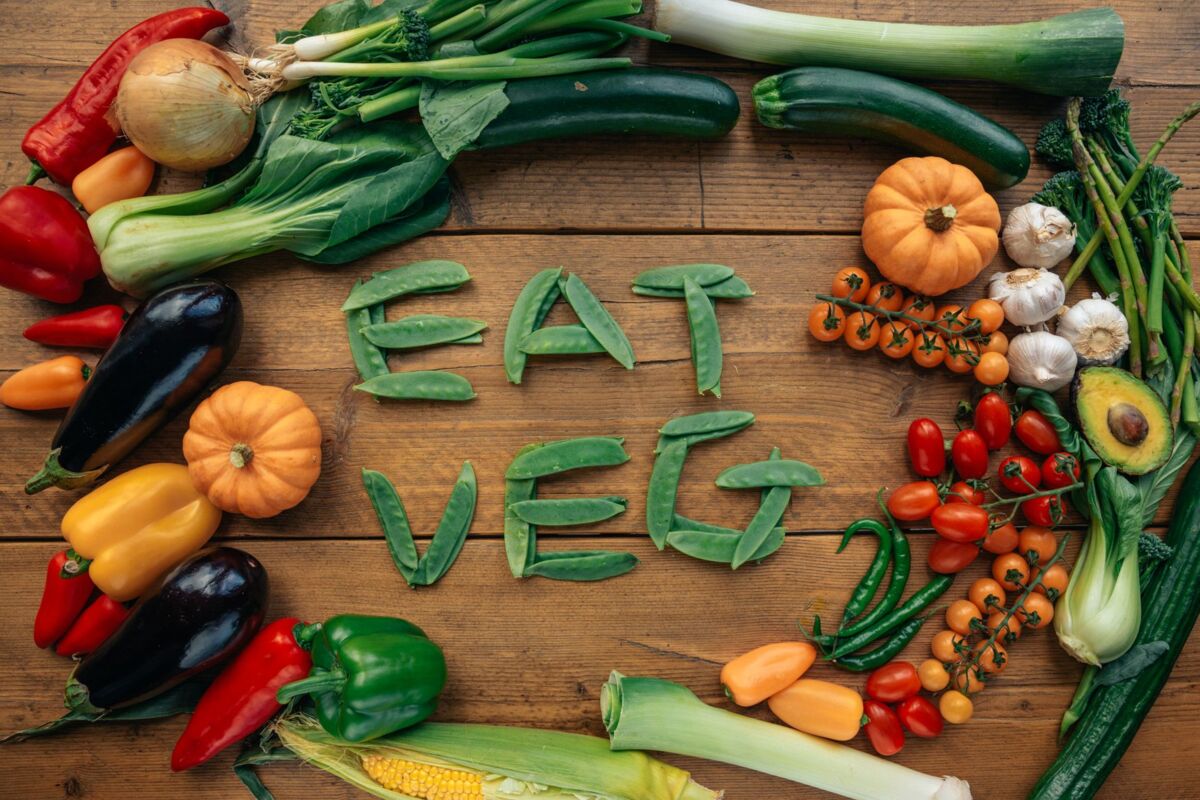 A vibrant flat lay of various fresh vegetables spelling 'Eat Veg' on a wooden background.