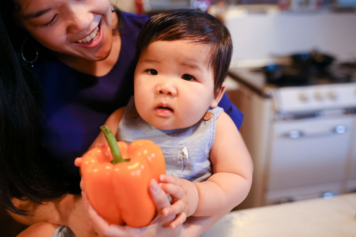 Asian mother and baby bonding in the kitchen with a fresh bell pepper.