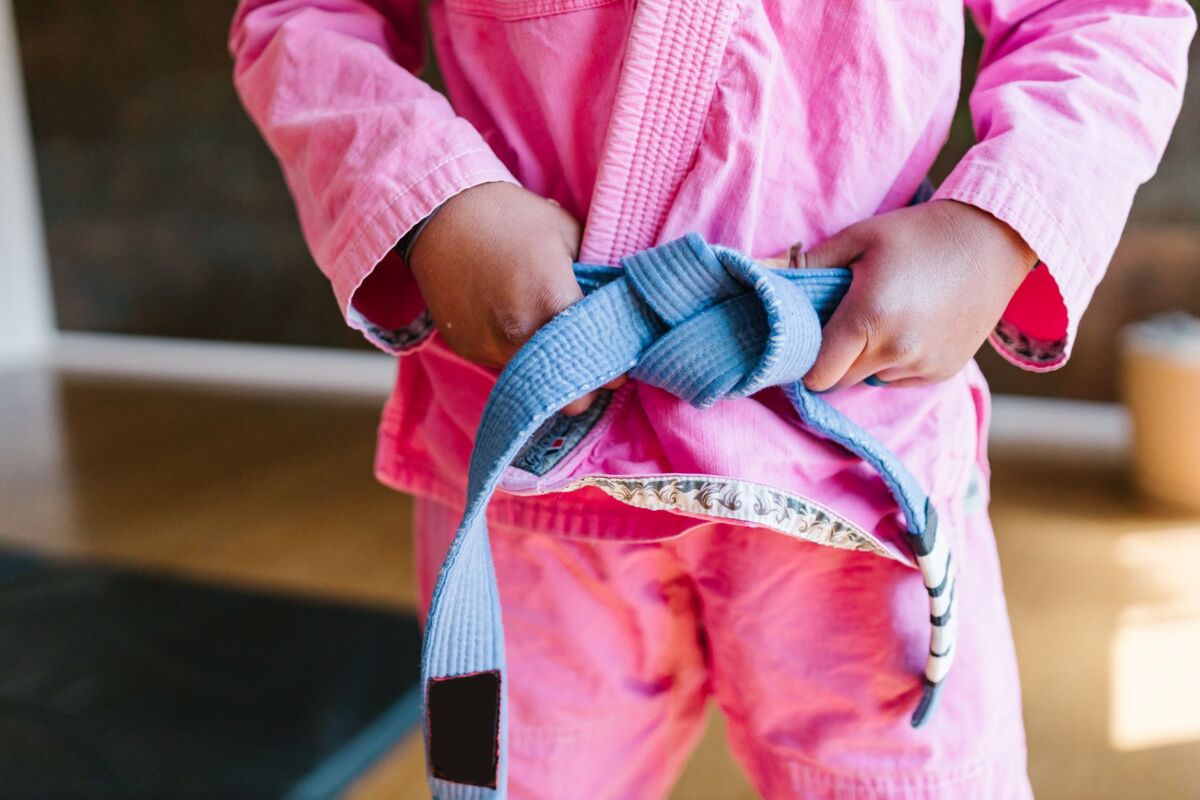 A child in a vibrant pink karate gi confidently tying a blue belt, symbolizing focus and discipline in martial arts.
